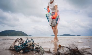 A female ecologist volunteer cleans the beach on the seashore from plastic and other waste.