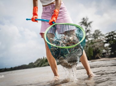 Kadın bir çevre bilimci plastikten ve diğer atıklardan sahil kenarını temizliyor..