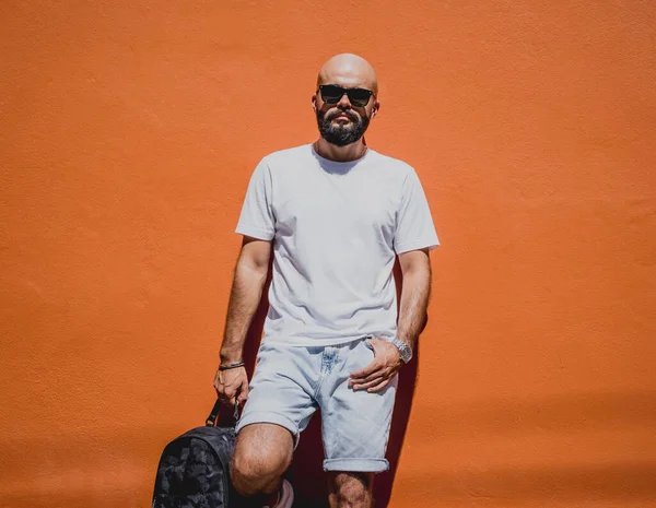 Male model with beard wearing white blank t-shirt on the background of an orange wall.