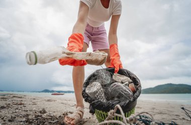 A female ecologist volunteer cleans the beach on the seashore from plastic and other waste.