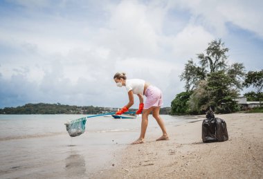 A female ecologist volunteer cleans the beach on the seashore from plastic and other waste.