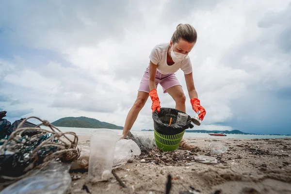 A female ecologist volunteer cleans the beach on the seashore from plastic and other waste.