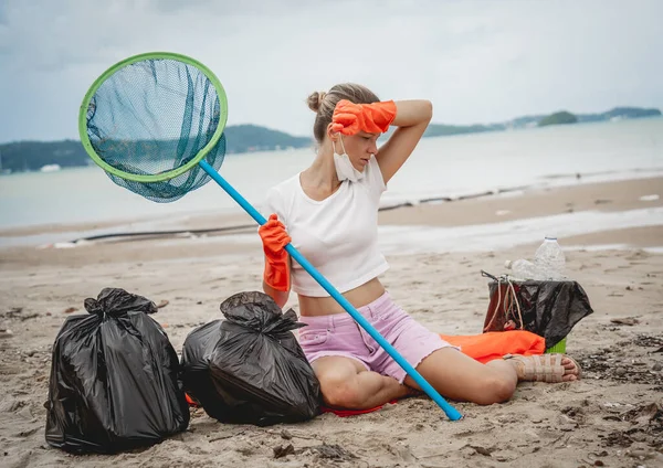 Plastik ve diğer atıklardan plajı temizledikten sonra bir kadın ekolojist dinleniyor..