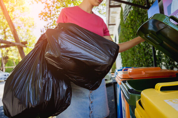 A young beautiful girl throws sorted garbage into special bins.