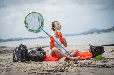A female ecologist volunteer is resting after cleaning the beach on the seashore from plastic and other waste.