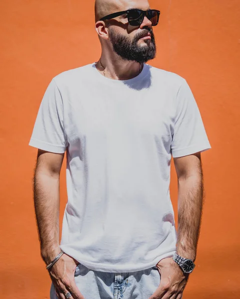 Male model with beard wearing white blank t-shirt on the background of an orange wall.