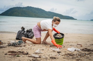 A female ecologist volunteer cleans the beach on the seashore from plastic and other waste.