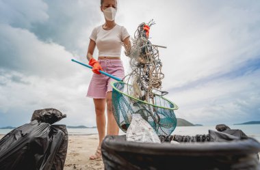 Kadın bir çevre bilimci plastikten ve diğer atıklardan sahil kenarını temizliyor..