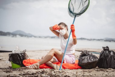 A female ecologist volunteer is resting after cleaning the beach on the seashore from plastic and other waste.