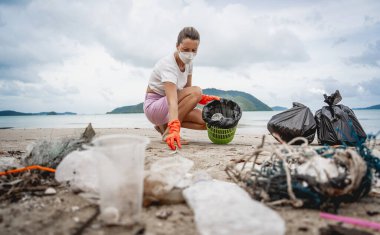 Kadın bir çevre bilimci plastikten ve diğer atıklardan sahil kenarını temizliyor..