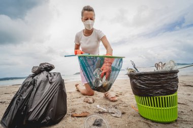 Kadın bir çevre bilimci plastikten ve diğer atıklardan sahil kenarını temizliyor..