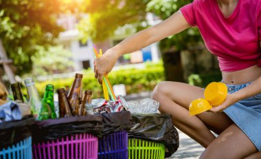Young beautiful girl sorts garbage into special bins.