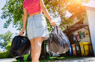 A young beautiful girl throws sorted garbage into special bins.