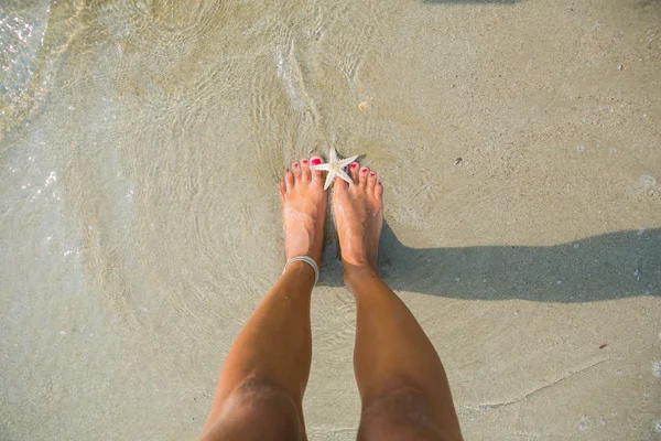 Pies humanos sobre arena con una estrella de mar — Foto de Stock