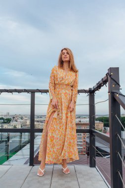 Uzun leopar desenli elbiseli güzel bir kadın bir binanın çatısında merdivenlerde dikiliyor..