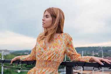 Uzun leopar desenli elbiseli güzel bir kadın bir binanın çatısında merdivenlerde dikiliyor..