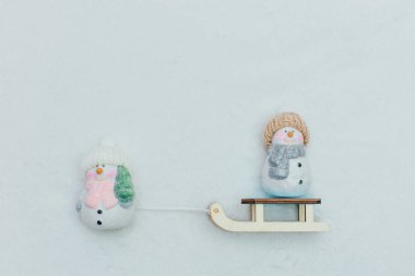 Dekoratif Noel temalı heykelcikler. Kızağın üzerinde örülmüş şapkalı iki kardan adam heykeli. Şenlikli dekor, sıcak bokeh ışıkları