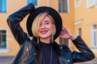 Sokak modası - açık havada şapka ve deri ceket giyen güzel bir kızın yakın plan portresi.