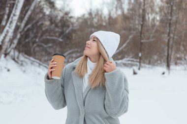 Karlı bir kış ormanında gülümseyen ve kahve içen güzel bir genç kız.