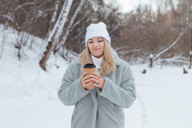 Karlı bir kış ormanında gülümseyen ve kahve içen güzel bir genç kız.