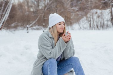 Güzel bir genç kız gülümser ve karlı bir kış ormanında kahve içmekten zevk alır.