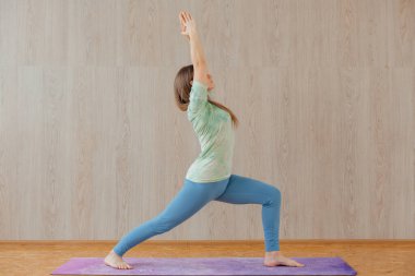 Mavi tayt ve tişört giymiş, evde yoga yapan beyaz bir kadın. Fitness ve sağlıklı yaşam tarzı konsepti.
