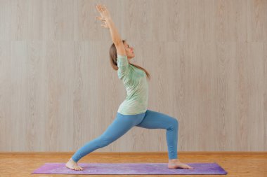 Mavi tayt ve tişört giymiş, evde yoga yapan beyaz bir kadın. Fitness ve sağlıklı yaşam tarzı konsepti.