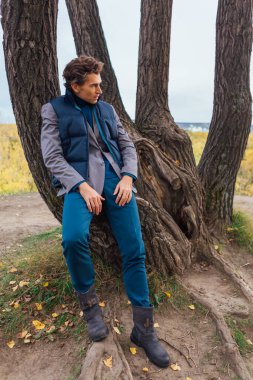 Sarı sonbahar ormanında ağacın yanında duran uzun boylu yakışıklı adam.