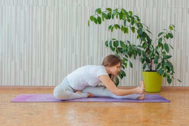 Mavi tayt ve tişört giymiş, evde yoga yapan beyaz bir kadın. Fitness ve sağlıklı yaşam tarzı konsepti.