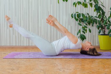 Mavi tayt ve tişört giymiş, evde yoga yapan beyaz bir kadın. Fitness ve sağlıklı yaşam tarzı konsepti.