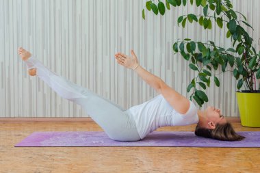 Mavi tayt ve tişört giymiş, evde yoga yapan beyaz bir kadın. Fitness ve sağlıklı yaşam tarzı konsepti.