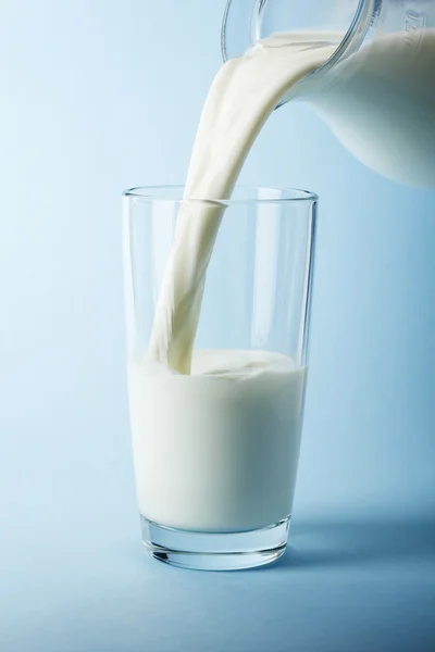 Gieten van melk in een glas geïsoleerd tegen blauwe achtergrond — Stockfoto