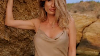 Deniz taşlarına poz veren çıplak elbiseli çekici bir kadının portresi. 
