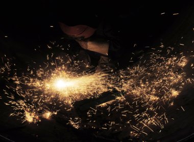 Metal ve kıvılcımlar üreten koruyucu maskeli kaynakçı.