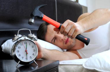 Lazy man is smashing the alarm clock with a hammer from the bed clipart
