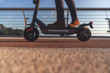 Takım elbiseli bir adamın kesilmiş görüntüsü ve şehrin caddesinde duran elektrikli scooter 'a basan ayakkabılar.