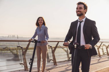 Genç iş adamı ve iş kadını şehrin arka planında elektrikli scooterlara binerken...