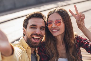 Genç çift bankta konuşarak ve selfie çekerek eğleniyor. Sabah şehirde yürürken telefonla..