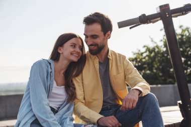 Genç bir çift bankta oturuyor ve rahatlıyor. Sabahları elektrikli scooterlara biniyorlar..