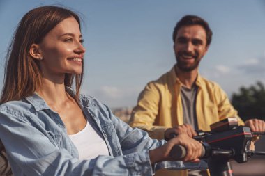 Genç ve neşeli bir çift yazın güneşli bir havada şehir parkında elektrikli scooter kullanıyor..