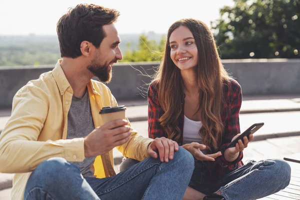 楽しい会話をしながらベンチに座ってコーヒーを飲みながら朝の街を歩いている若いカップル — ストック写真