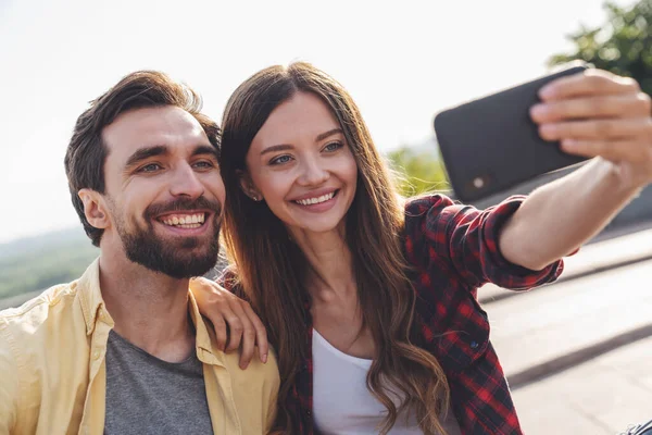 Genç çift bankta konuşarak ve selfie çekerek eğleniyor. Sabah şehirde yürürken telefonla..