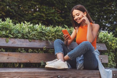 Bir yaz parkında bankta oturmuş video konferansı sırasında sohbet eden güzel bir kız..