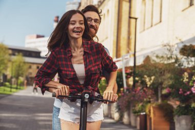Şehrin caddesinde elektrikli scooter kullanan neşeli genç bir çift..