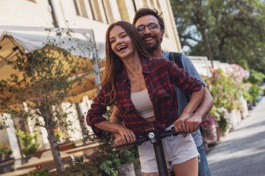 Şehrin caddesinde elektrikli scooter kullanan neşeli genç bir çift..