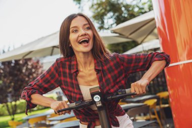 Şehrin caddesinde elektrikli scooter sürerken neşeli, genç ve güzel bir kız..