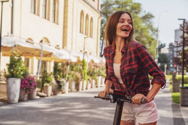 Şehrin caddesinde elektrikli scooter sürerken neşeli, genç ve güzel bir kız..