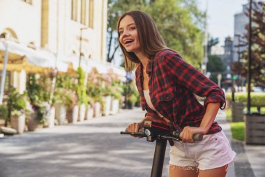 Şehrin caddesinde elektrikli scooter sürerken neşeli, genç ve güzel bir kız..