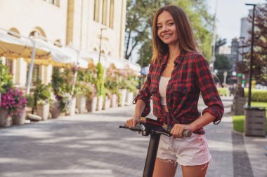 Şehrin caddesinde elektrikli scooter sürerken neşeli, genç ve güzel bir kız..