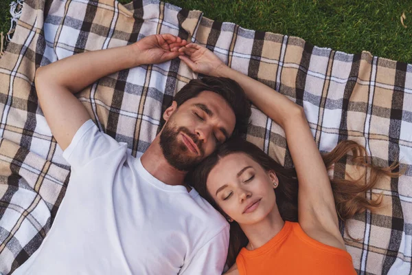 ピクニック中に公園の毛布の上に寝そべっている若い陽気なカップル トップビュー — ストック写真